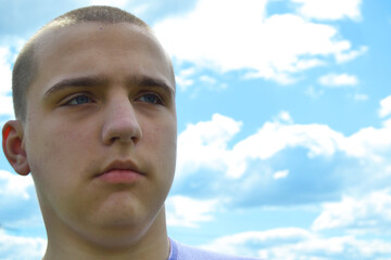 Young handsome autistic guy looks into the distance against the blue sky