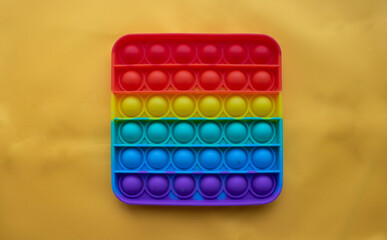 A rainbow toy lies against a background of yellow fabric. Blue and Orange Funny Interactive Anti-Stress Silicone Toys. Pop it