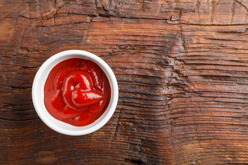 White gravy boat with ketchup on a wooden table.