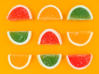 Multicolored marmalade citrus slices in sugar on orange background.