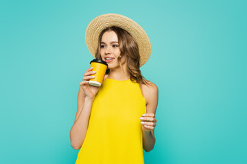 Pretty woman in straw hat holding takeaway drink isolated on blue