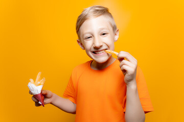 a boy in an orange T shirt holds a bag of deep fried potatoes in front of him and bites one piece...