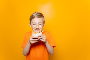 a boy in an orange T-shirt holds a bag of deep-fried potatoes in front of him and sniffs it with his eyes closed