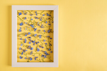 Floral pattern made of blue flowers and frame on a yellow background. Top view, copy space.