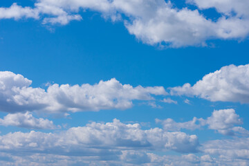 A lot of white fluffy cumulus clouds on bright summer blue sky far to horizon. Cloudscape, overcast.