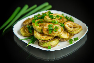 fried zucchini in circles with fresh herbs in a plate on a black