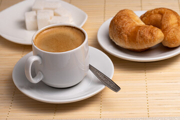 coffee with two fresh croissants on a white plate and a few pieces of sugar on a napkin made of natural bamboo