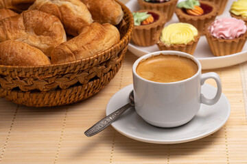 coffee with fresh croissants in a wicker basket and cakes on a white plate on a napkin made of natural bamboo