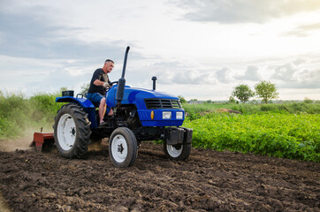 Obraz premium Farmer on tractor cultivates farm field. Milling soil, crushing and loosening ground before cutting rows. Farming, agriculture. Preparatory earthworks before planting a new crop. Land cultivation