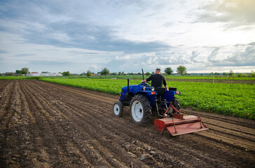 Farmer on tractor cultivates farm field. Milling soil, crumbling ground before cutting rows....
