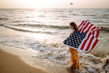 Young woman with american flag on the beach at sunset. 4th of July. Independence Day. Patriotic...