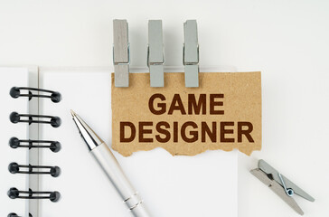 On a white background lies a notebook, a pen, clothespins and cardboard with the inscription - Game Designer