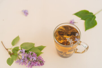 Lilac, purple flowers in a glass with tea on a yellow modern background. Concept, heat, quench your thirst, summer vacation, there is a place for text