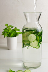 Fresh water infused with cucumbers and mint sprigs, detox drink. Water is poured into the jug. Health care, fitness, healthy food concept.