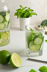 A glass of detox water infused with cucumber and mint, with a jug and ingredients. Health care, fitness, healthy food concept.
