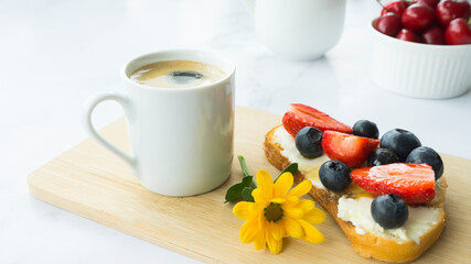 Cup of coffee, toast with mascarpone cheese and berries, beautiful yellow flower. Breakfast concept. Image with selective focus