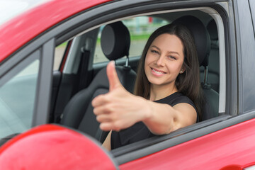 Naklejka na ściany i meble Car. Beautiful woman in the car shows thumbs up. Happy brunette in the car.