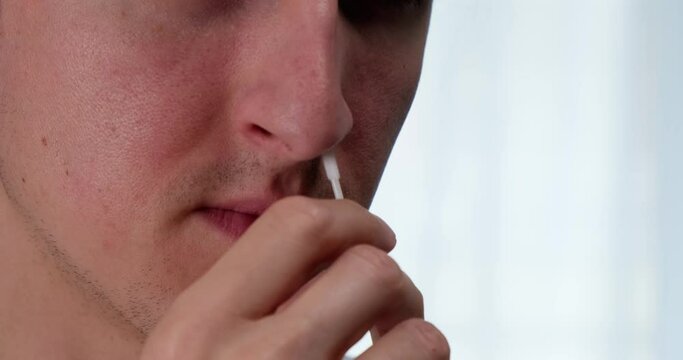 Close up of man inserting nasal swab into the nostril to take a rapid antigen self test for Coronavirus.