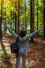 Woman tourist hiker walking through forest in Carpathian mountains enjoying view. Happy traveler raising arms