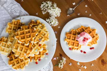 Homemade viennese waffles with fresh strawberries and ice cream on white plates on white tablecloth and white lilac branches and flowers on wooden table