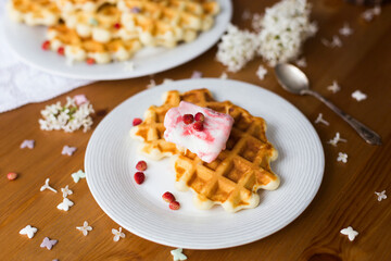 Homemade viennese waffles with fresh strawberries and ice cream on white plates on white tablecloth and white lilac branches and flowers on wooden table