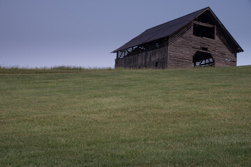 Old weathered barn with nothing but blue sky and green grass. Minimalism.
