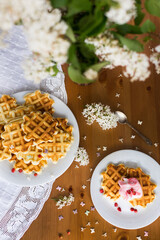 Homemade viennese waffles with fresh strawberries and ice cream on white plates on white tablecloth and white lilac branches and flowers on wooden table