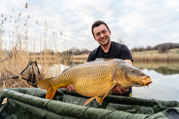 Fisherman holding a huge carp at the lake.