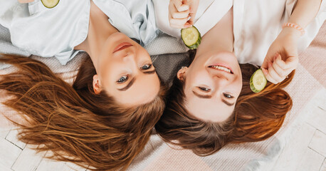 Two girls make homemade face and hair beauty masks. Cucumbers for the freshness of the skin around...
