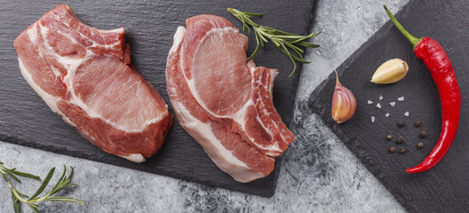Raw pork steak on a dark background with herbs.