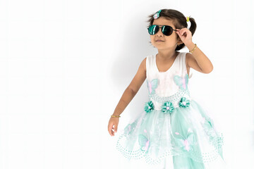 Close up of nice little indian girl with pony tail and dark sunglass , smiles and looks away, Stands over white background with copy space on the left side, Studio shot
