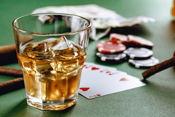Glass of whiskey, cigar, playing cards and chips on green background