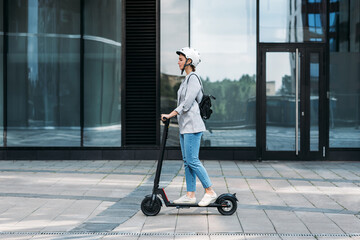 Side view of a young businesswoman riding electric push scooter. Female in cycling helmet driving...