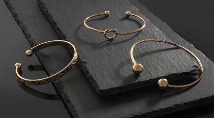 Fototapeta na wymiar Three modern design golden bracelets on natural black stone plates