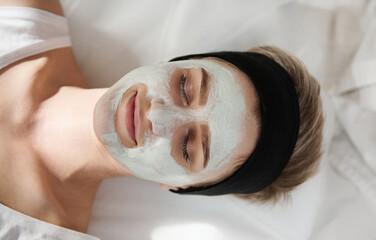 Top view of a happy young woman with a beauty mask on her face relaxing and enjoying beauty procedure in spa salon
