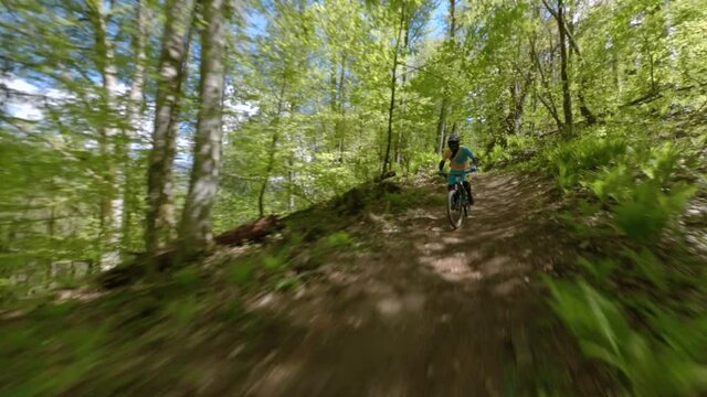 Shooting from sport fpv drone active male rider driving on downhill bike at natural forest bikepark with green trees and grass. Aerial shot sportsman riding mtb on trail enjoy extreme activity outdoor