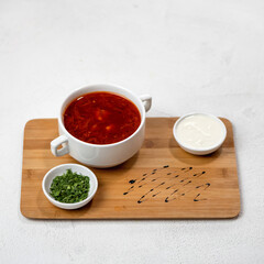 Red soup or borscht with greens and sour cream. Pot of tomato soup with meat and beets on cutting board. Isolated on white background. Served lunch. Nutritious food. Delicious and healthy dinner.