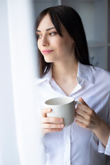 Portrait of a relaxing young beautiful brunette woman drinking coffee near the window.