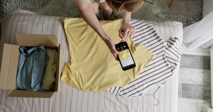Woman taking photo of used shirt to sell online, second hand clothes resale or donation concept, sustainable living, pre owned clothing.