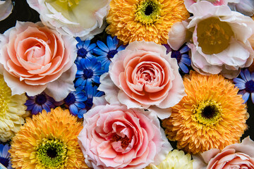 Flower arrangement of pink roses and yellow mums floating on the water.