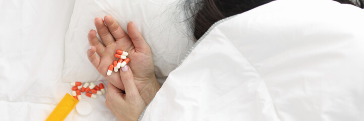 Woman's hand sticks out from under blanket, pills lie on her hand.