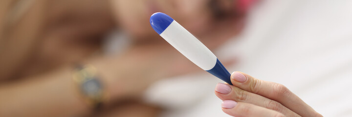 Woman lies on bed and holds thermometer