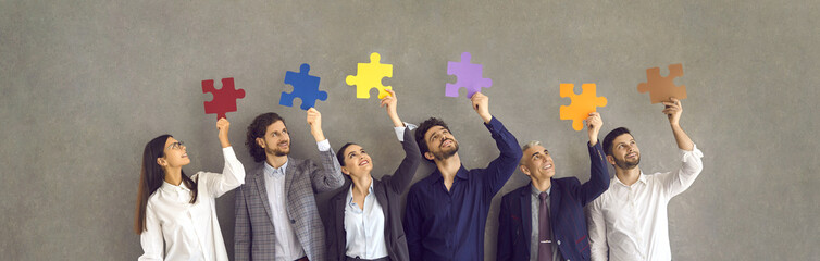 Team of happy business people standing in row holding colorful jigsaw pieces. Group of smiling...