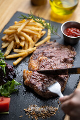 cutting steak with knife and fork on black plate