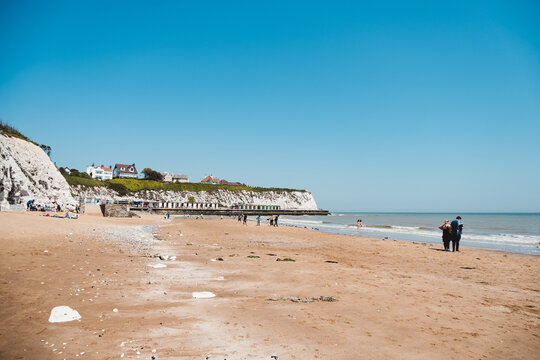 People chilling at Dumpton Gap bay with colourful wooden beach huts between Broadstairs and Ramsgate