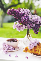 Obraz na płótnie Canvas Cup of tea with lilac flowers and french croissant