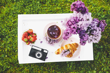 Photo camera and lilac flowers with french croissant and strawberry. Beautiful breakfast with coffee. Top view