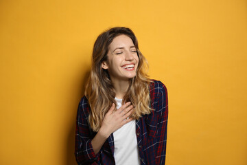 Cheerful young woman laughing on yellow background