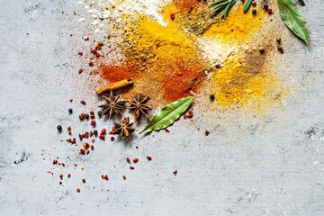 Various spice powders (paprika, curry, coriander, ginger, dried onions and garlic, turmeric, cinnamon, pepper, anise) and herbs (rosemary, bay leaf) on gray background. Indian and Asian cuisine.