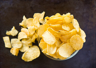 Crispy potato chips in a plate on metallic black grunge background